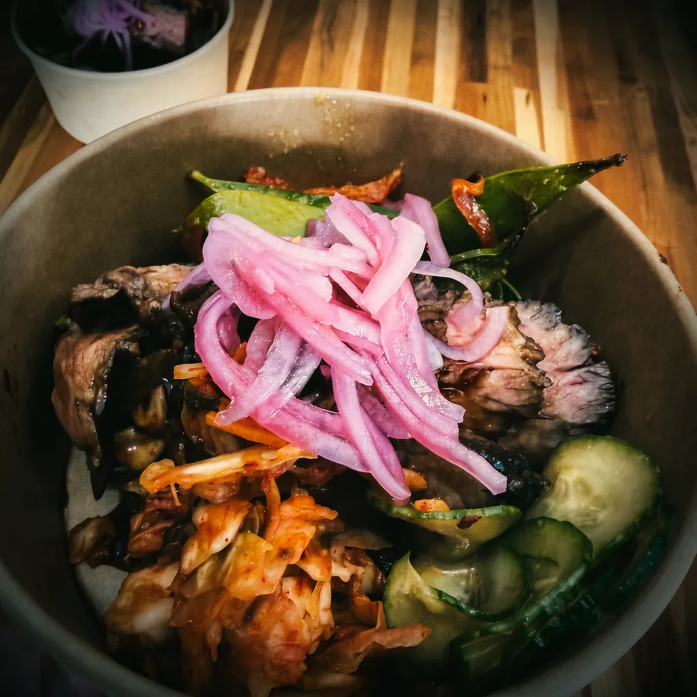 A sliced steak bowl with kimchi and pickled onions